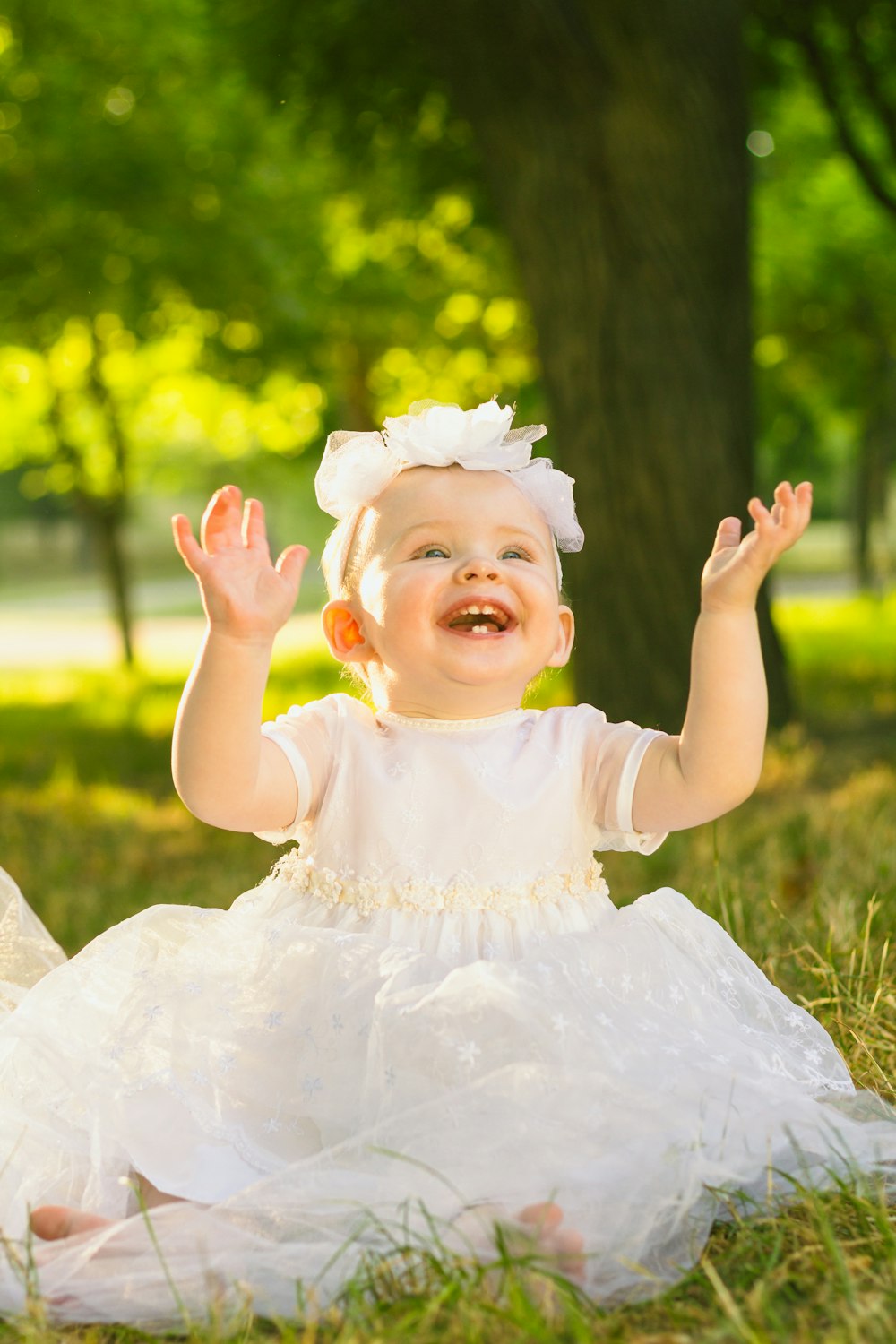 a baby girl in a white dress sitting in the grass