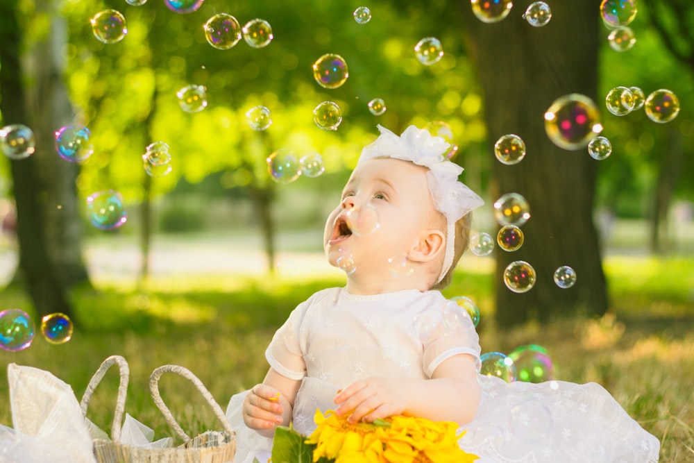 a baby sitting in the grass with bubbles in the air