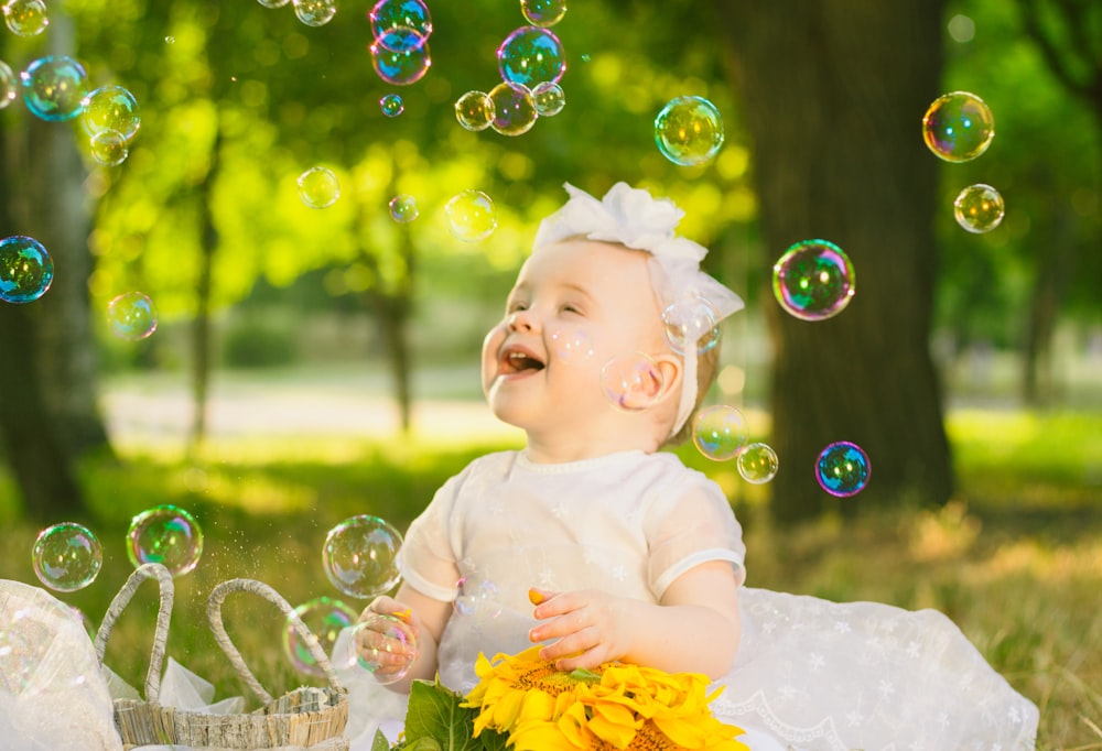 a baby girl in a white dress sitting in the grass