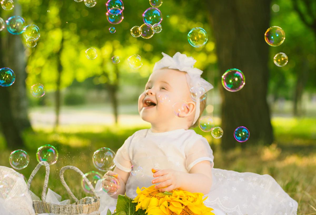 A baby girl sitting in a green meadow wearing a white natural cotton dress, enjoying the outdoors