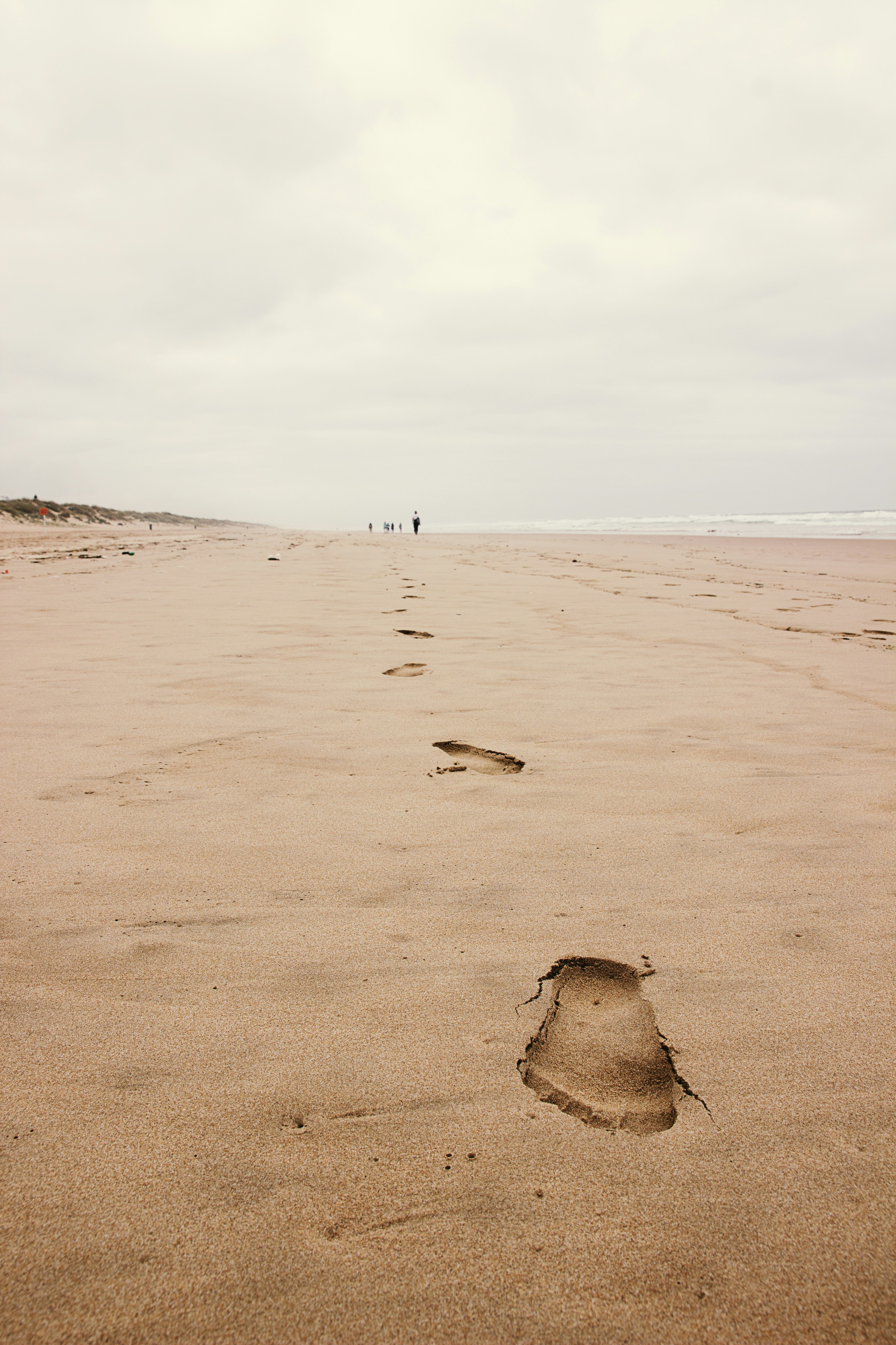 um par de pessoas andando através de uma praia de areia