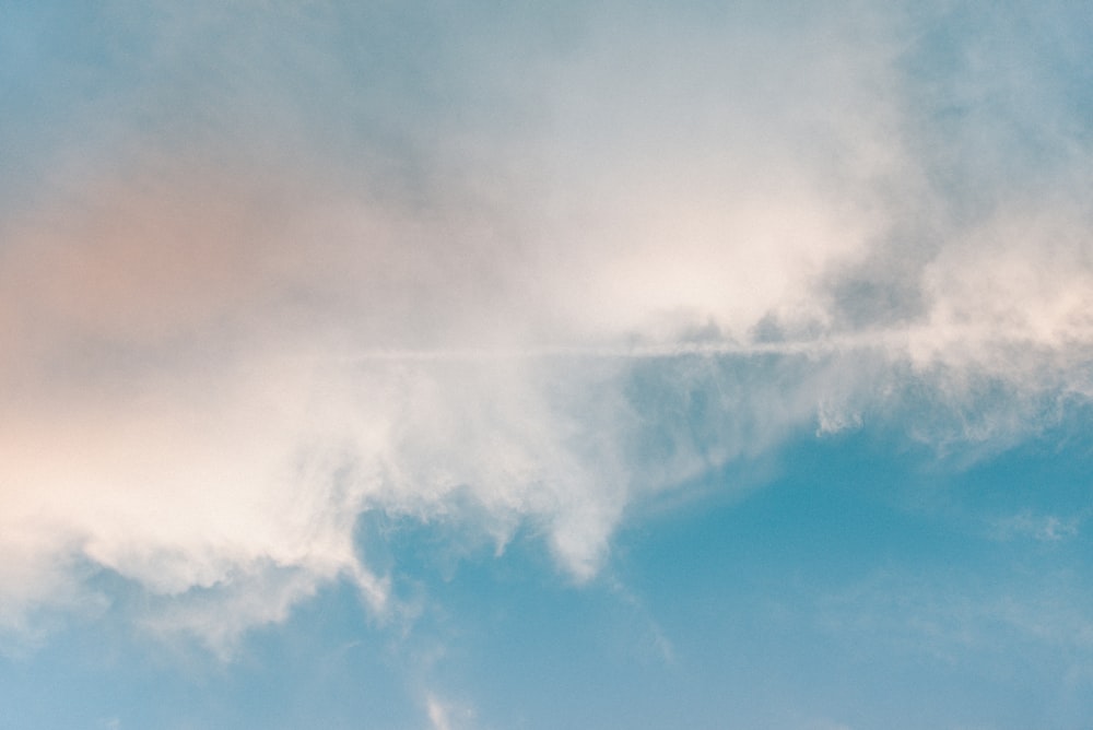 a jet flying through a cloudy blue sky