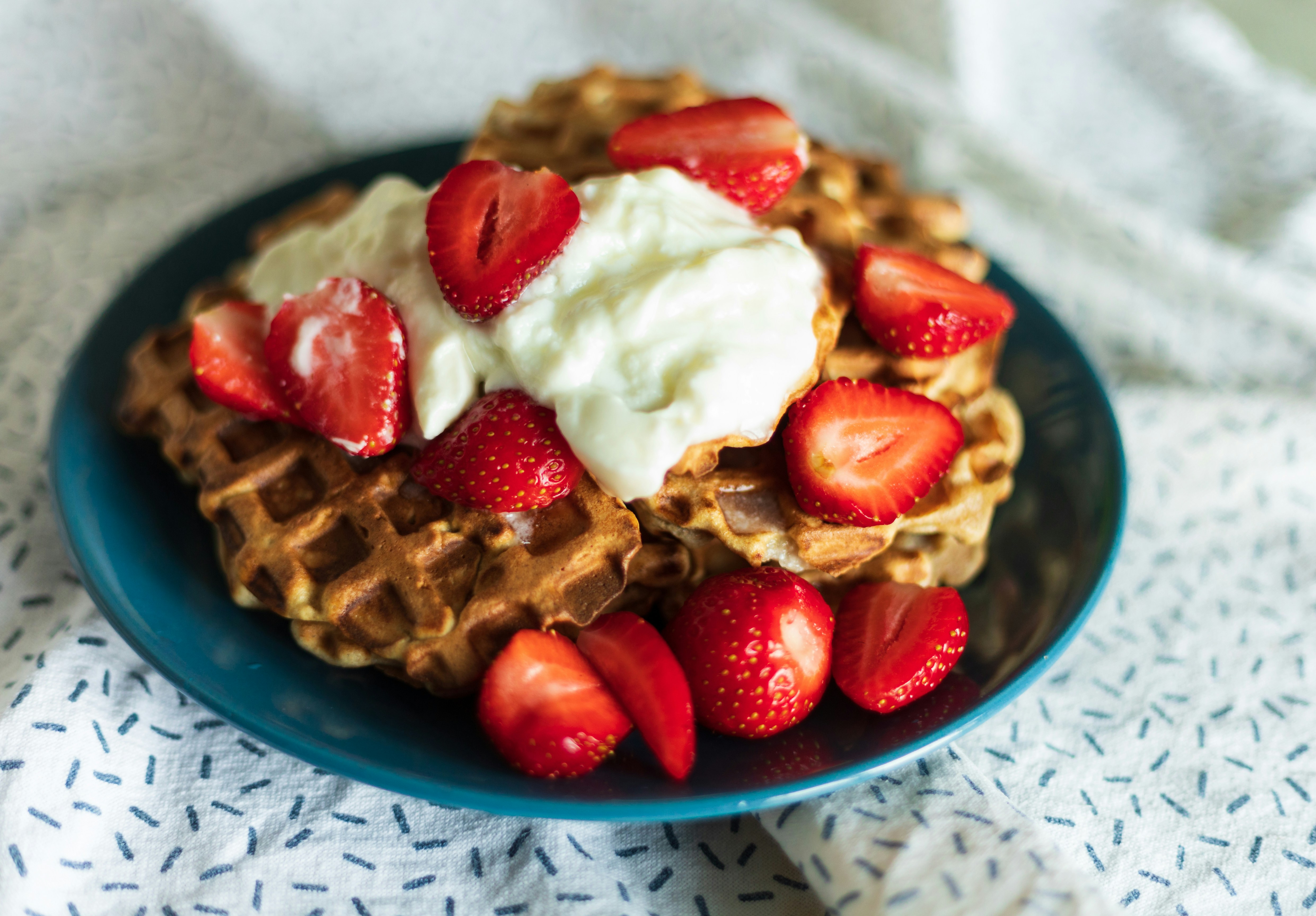 a blue plate topped with waffles covered in whipped cream and strawberries
