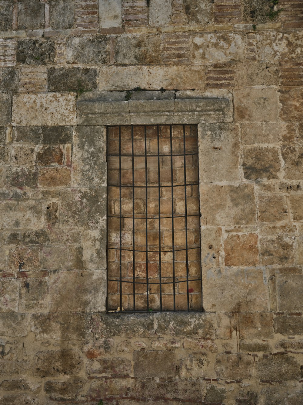 una pared de ladrillo con una ventana y rejas