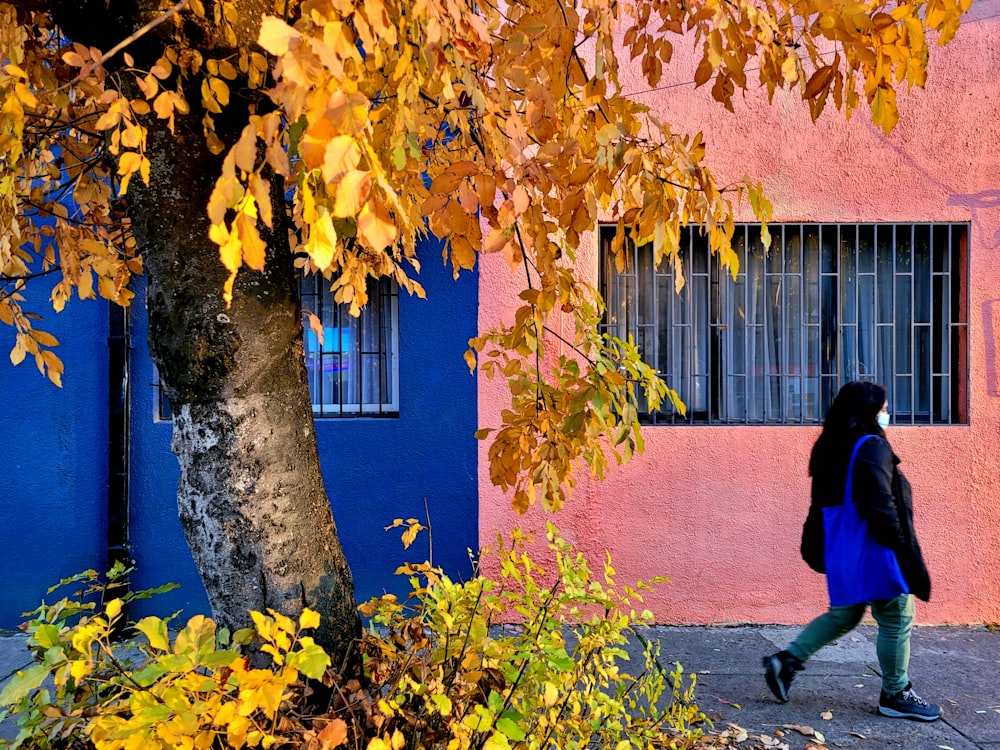 a woman walking down a sidewalk next to a tree
