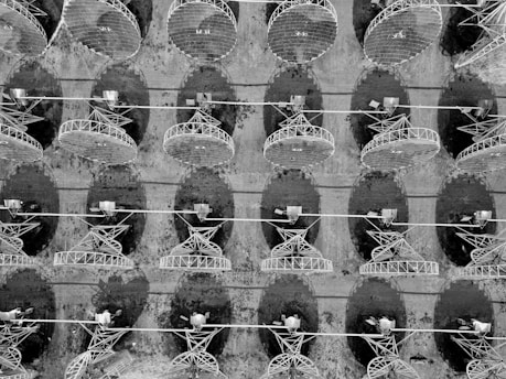 An array of large satellite dishes arranged in a grid-like pattern, viewed from above. The shadows of the dishes cast dark oval shapes on the ground, and the metal framework is clearly visible.
