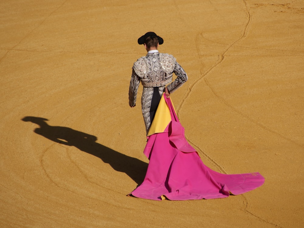 a woman in a pink and yellow dress standing in a desert