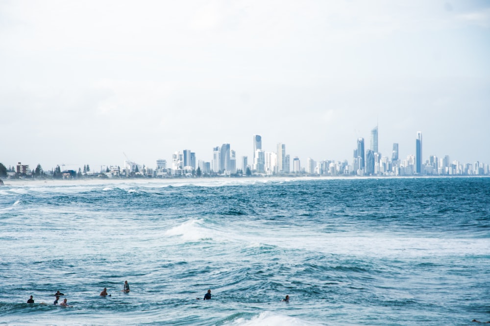 a group of people swimming in the ocean with a city in the background