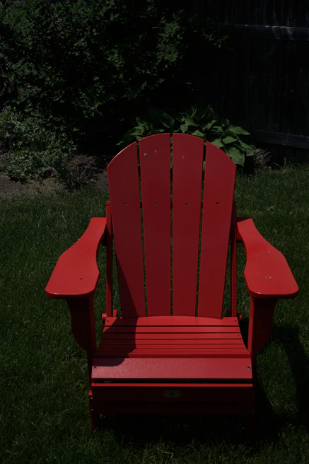 A vibrant plastic outdoor Adirondack chair placed on a sunlit wooden deck surrounded by greenery.