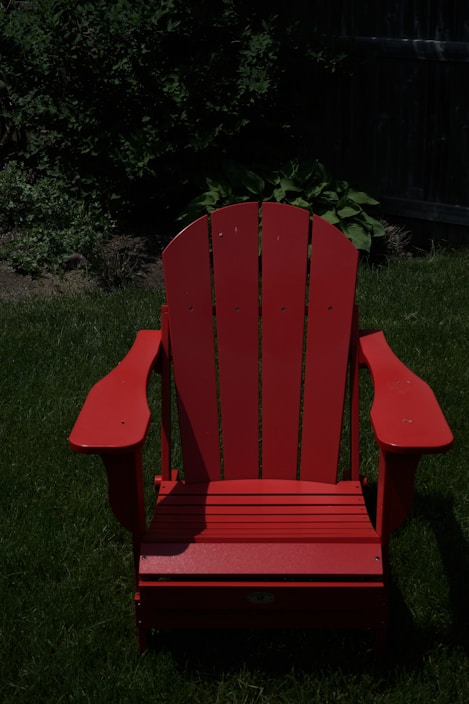 A bright plastic outdoor Adirondack chair set on a sunny patio surrounded by lush greenery.