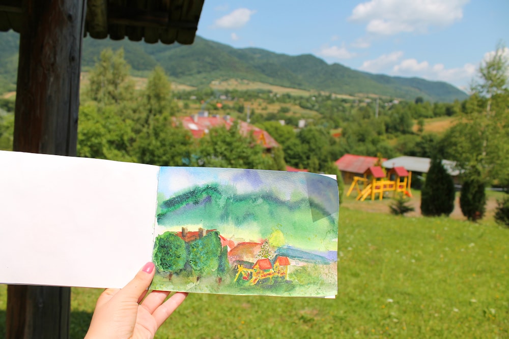 a person holding a piece of paper with a painting on it