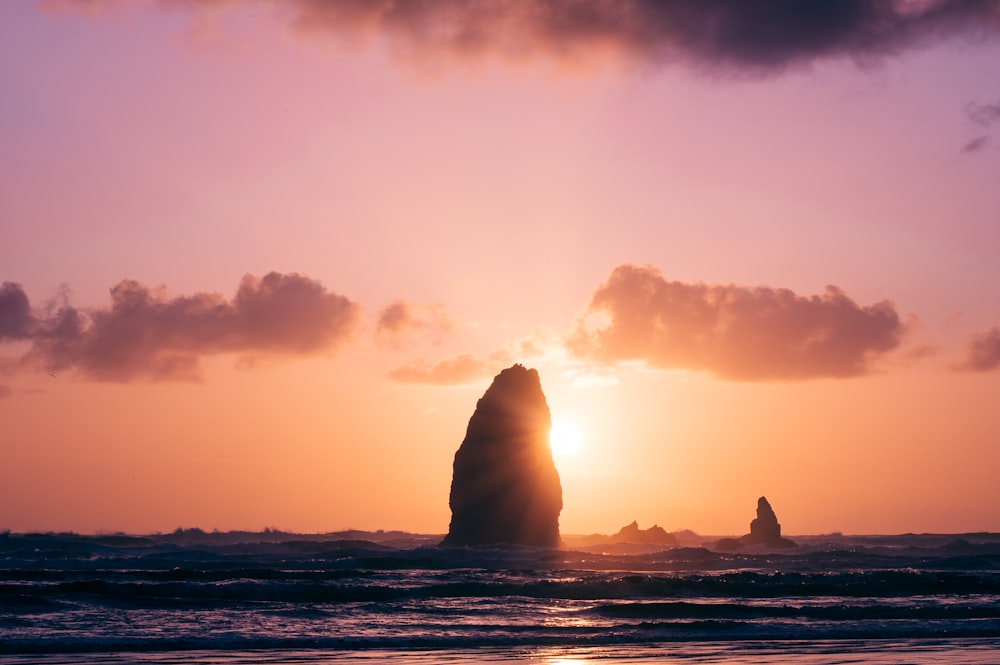 the sun is setting behind a large rock in the ocean