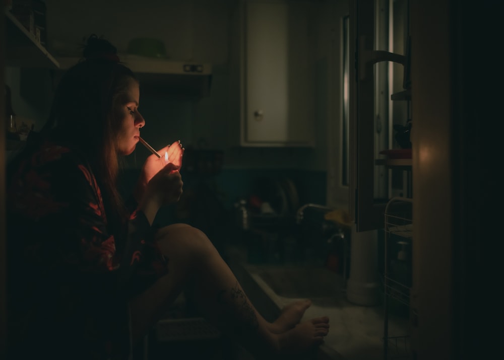 a woman sitting on a kitchen counter smoking a cigarette