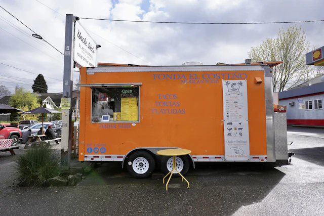 The bright orange Curb food truck parked on a city street with its serving window open
