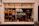 A bakery storefront with a large window displaying an assortment of bread and baked goods. The glass is adorned with the logo 'WILD DOUGH' along with the tagline 'REAL BREAD - REAL FOOD - LOCALLY SOURCED'. Inside, there are several shelves with loaves of bread and pastries. The atmosphere suggests a welcoming and artisanal vibe, further highlighted by warm lighting from hanging lamps.
