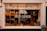 A bakery storefront with a large window displaying an assortment of bread and baked goods. The glass is adorned with the logo 'WILD DOUGH' along with the tagline 'REAL BREAD - REAL FOOD - LOCALLY SOURCED'. Inside, there are several shelves with loaves of bread and pastries. The atmosphere suggests a welcoming and artisanal vibe, further highlighted by warm lighting from hanging lamps.