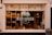 A bakery storefront with a large window displaying an assortment of bread and baked goods. The glass is adorned with the logo 'WILD DOUGH' along with the tagline 'REAL BREAD - REAL FOOD - LOCALLY SOURCED'. Inside, there are several shelves with loaves of bread and pastries. The atmosphere suggests a welcoming and artisanal vibe, further highlighted by warm lighting from hanging lamps.