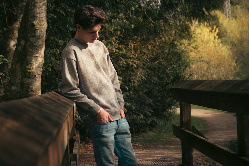 a young man standing on a bridge next to a forest