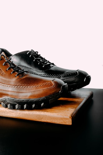 a pair of black and brown shoes sitting on top of a wooden board