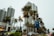 Tall modern buildings surrounded by palm trees line a street. A green Jeep is parked alongside other vehicles. A blue directional sign points towards Miami Beach Marina and South Pointe Park. The sky is overcast, creating a subdued atmosphere.