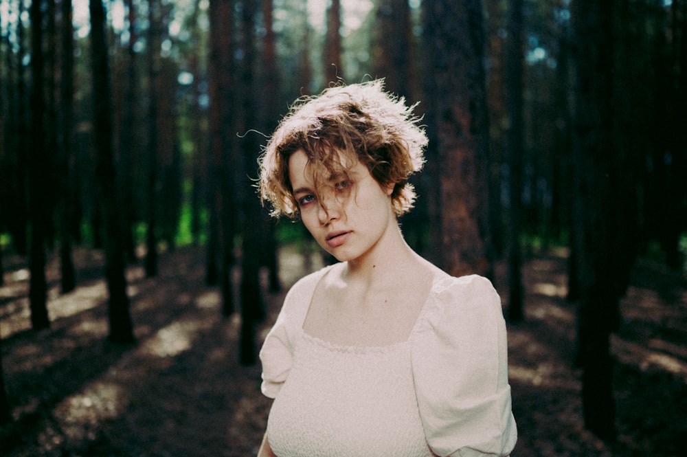 a woman in a white dress standing in a forest