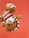 A plush toy resembling an animal is being held upside down against a solid red background. The toy is light brown with a white and red striped outfit, including a matching cap. Its black button-like eyes and round nose give it a cute, playful appearance.