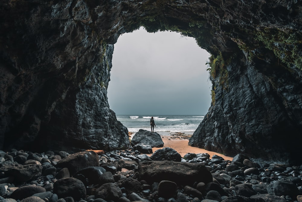 a person standing in a cave on a rocky beach