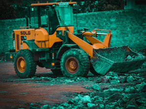 A yellow backhoe loader ready for work near a stone wall