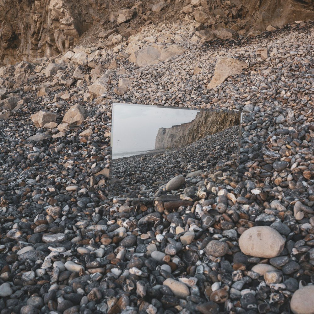 a mirror sitting on top of a rocky beach