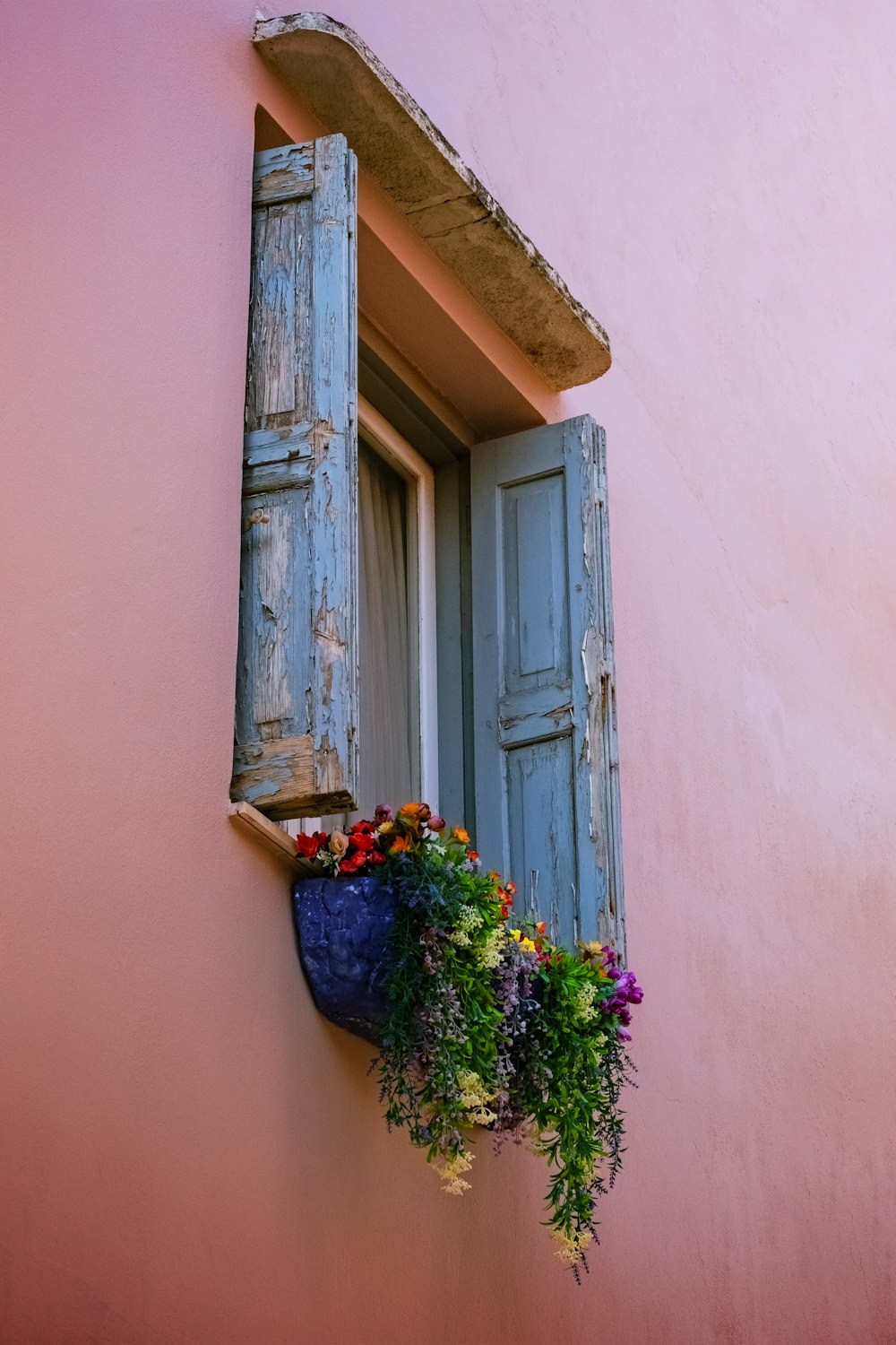 a window with blue shutters and a blue planter filled with flowers