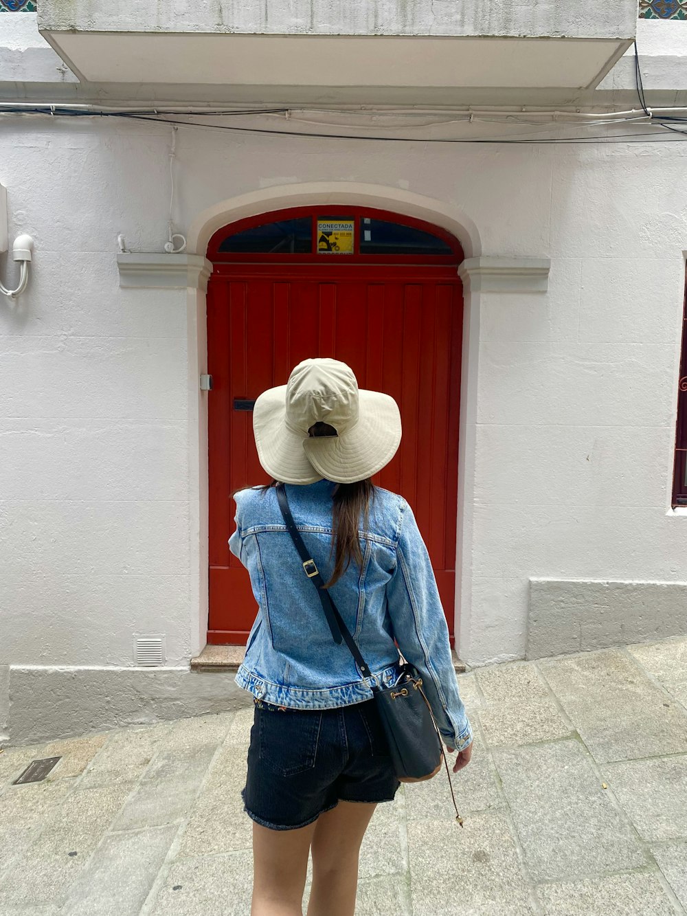 a woman wearing a hat and denim jacket standing in front of a red door