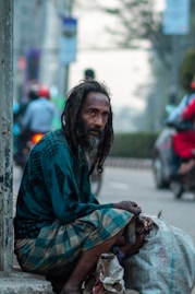a man with dreadlocks sitting on a curb