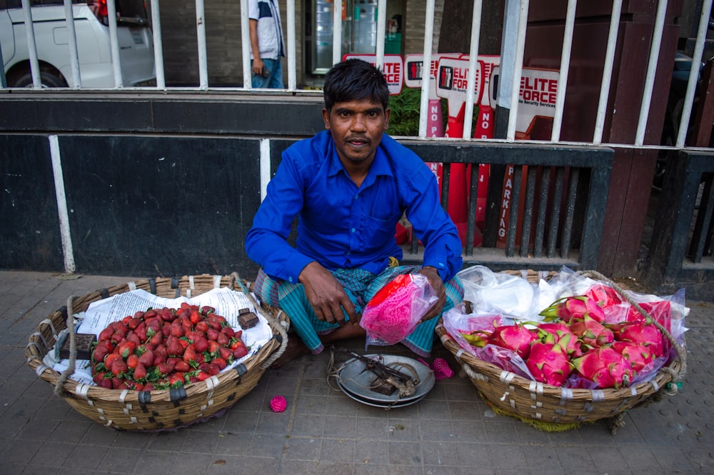 a man sitting in front of baskets of strawberries