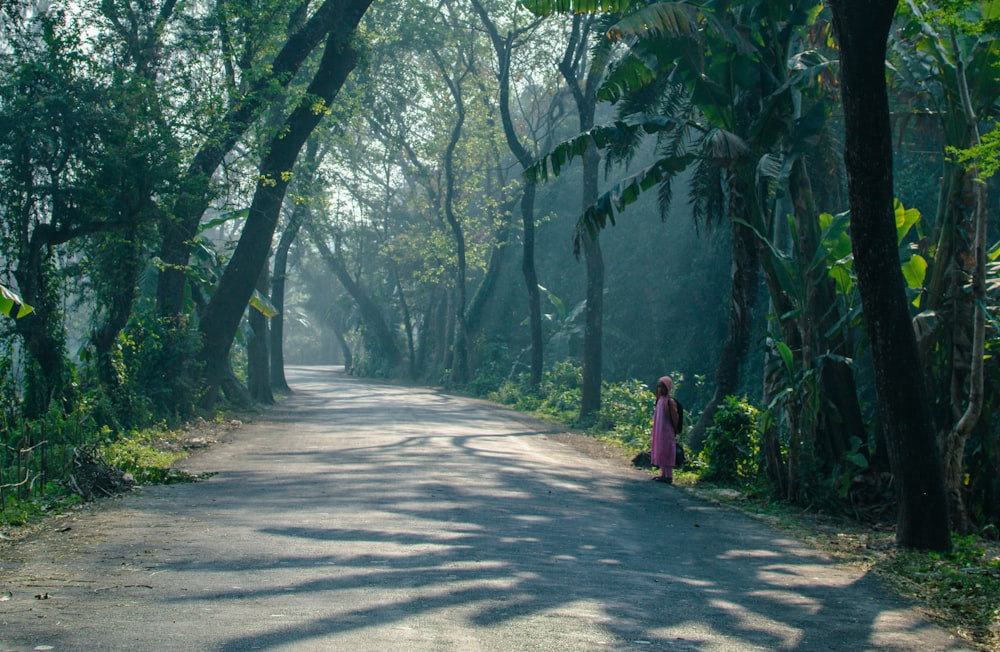 a woman walking down a road in the middle of a forest