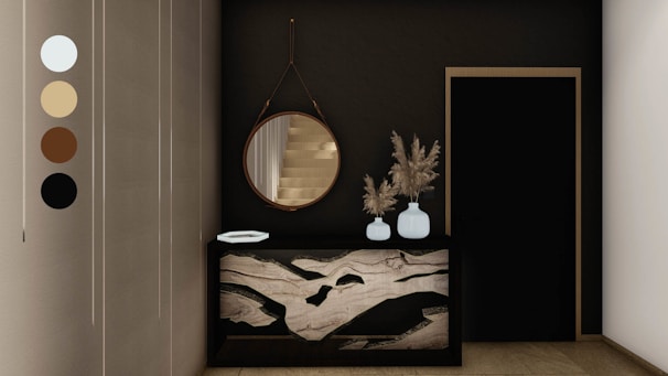 An elegant and modern interior space featuring a dark wall with a round mirror hanging above a decorative console table. The table has a unique marble design and holds two white vases filled with dried pampas grass. Next to it is a black door with a simple frame. Neutral tones are present, accentuated by the sleek design elements.