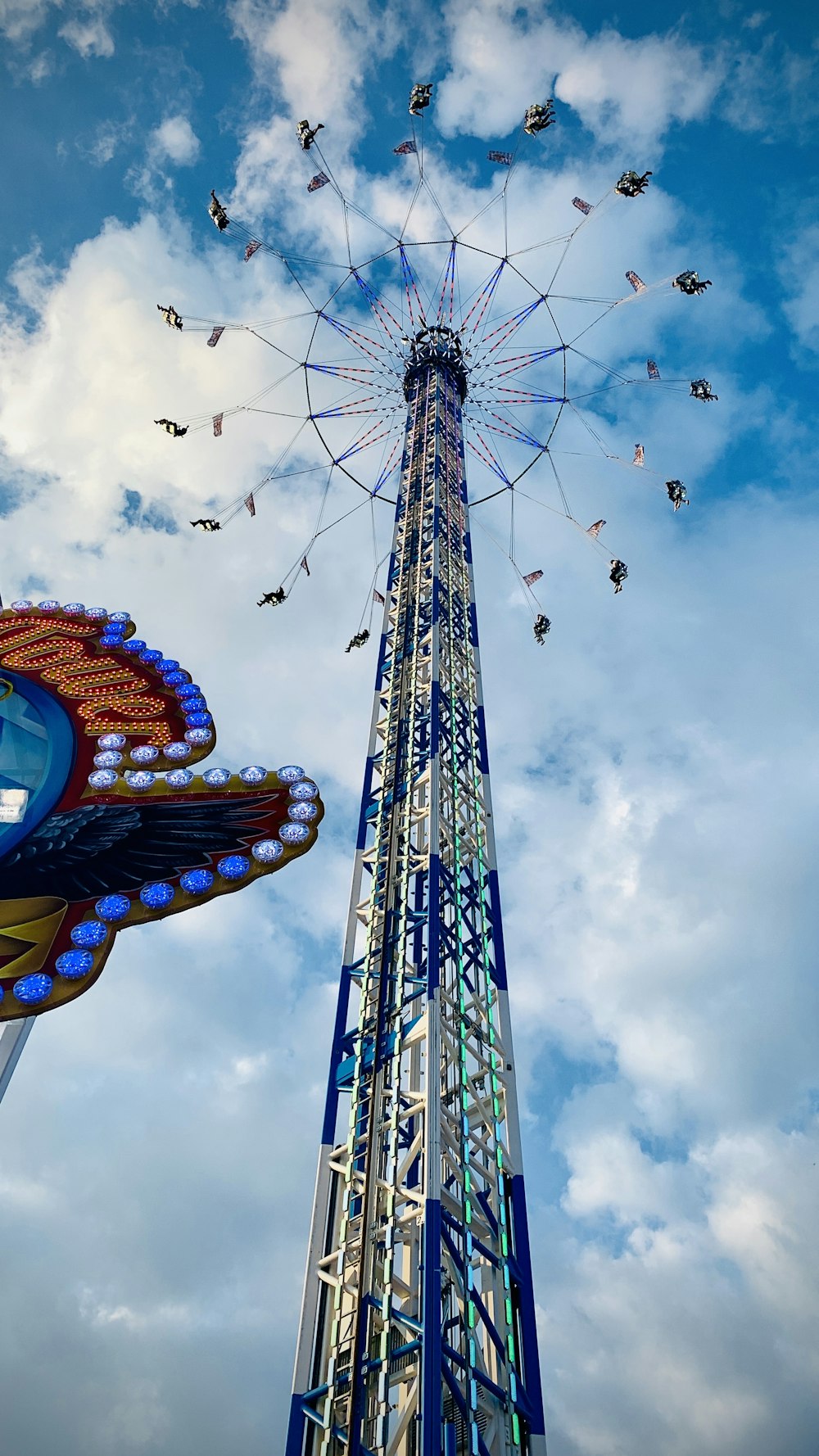a ferris wheel and a carnival ride against a cloudy blue sky