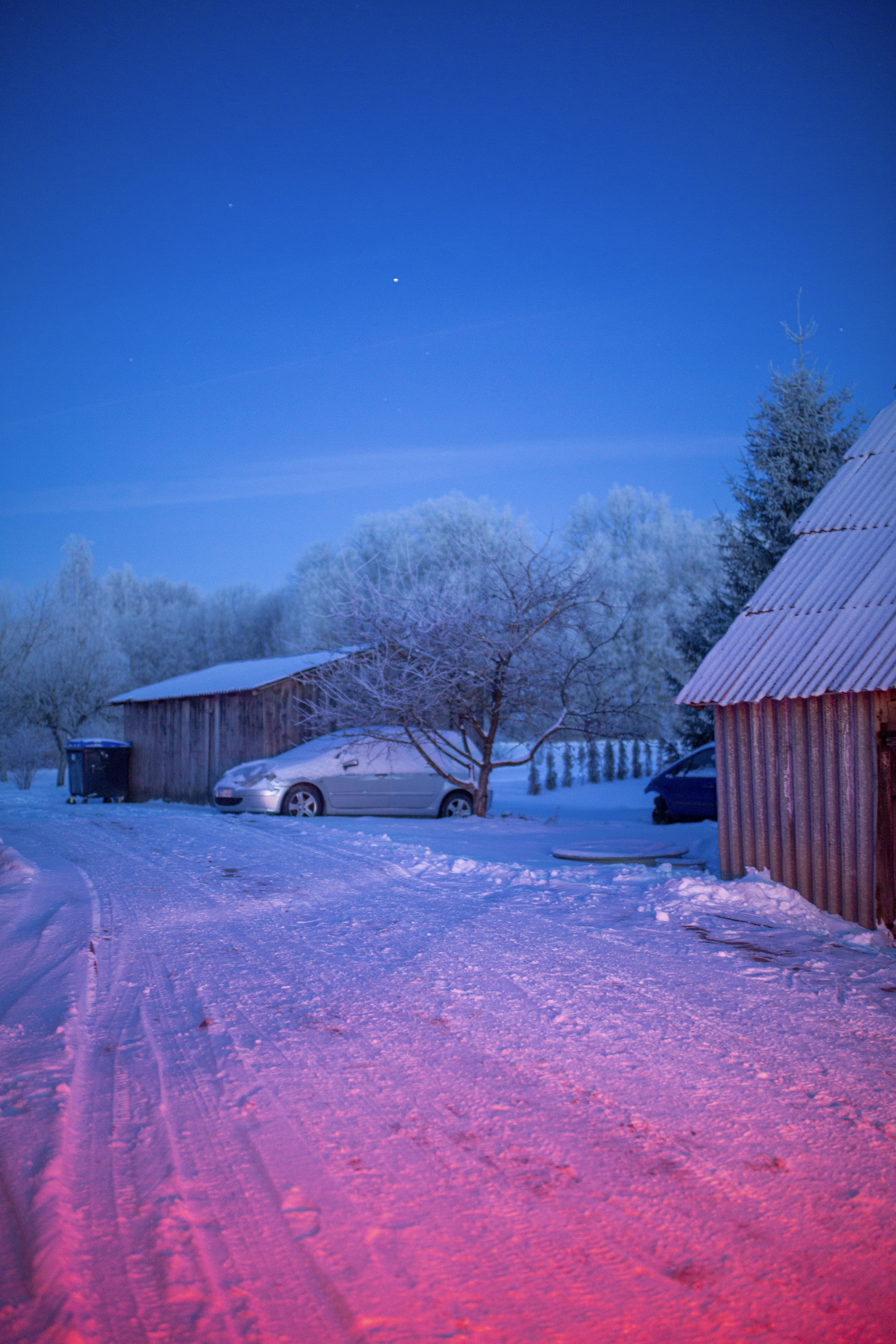 a snow covered road with a barn and a car in the background