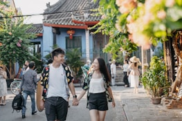 A happy couple holding hands, smiling under a floral arch at sunset.