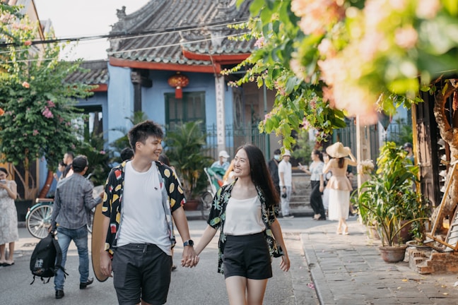 A couple smiling and holding hands while walking in a sunlit park.
