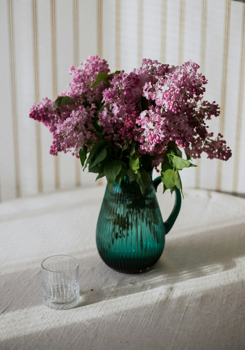 a green vase filled with purple flowers on top of a table