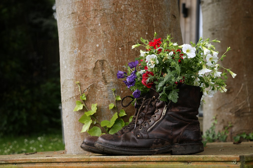 a pair of boots with flowers in them sitting next to a tree