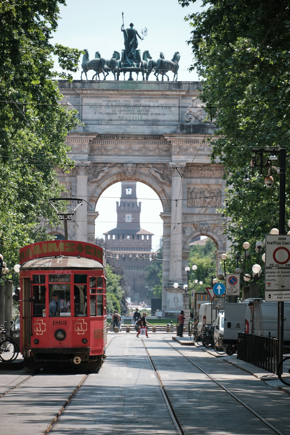 a red trolley driving down a street next to a tall arch