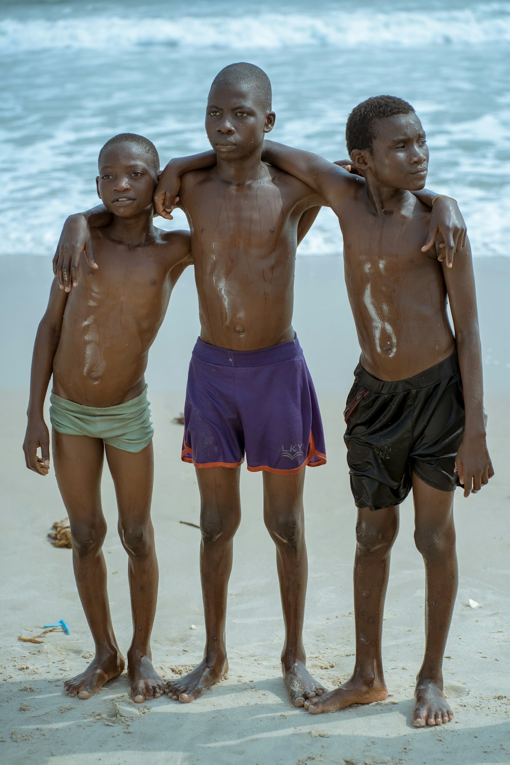 a group of three boys standing next to each other on a beach