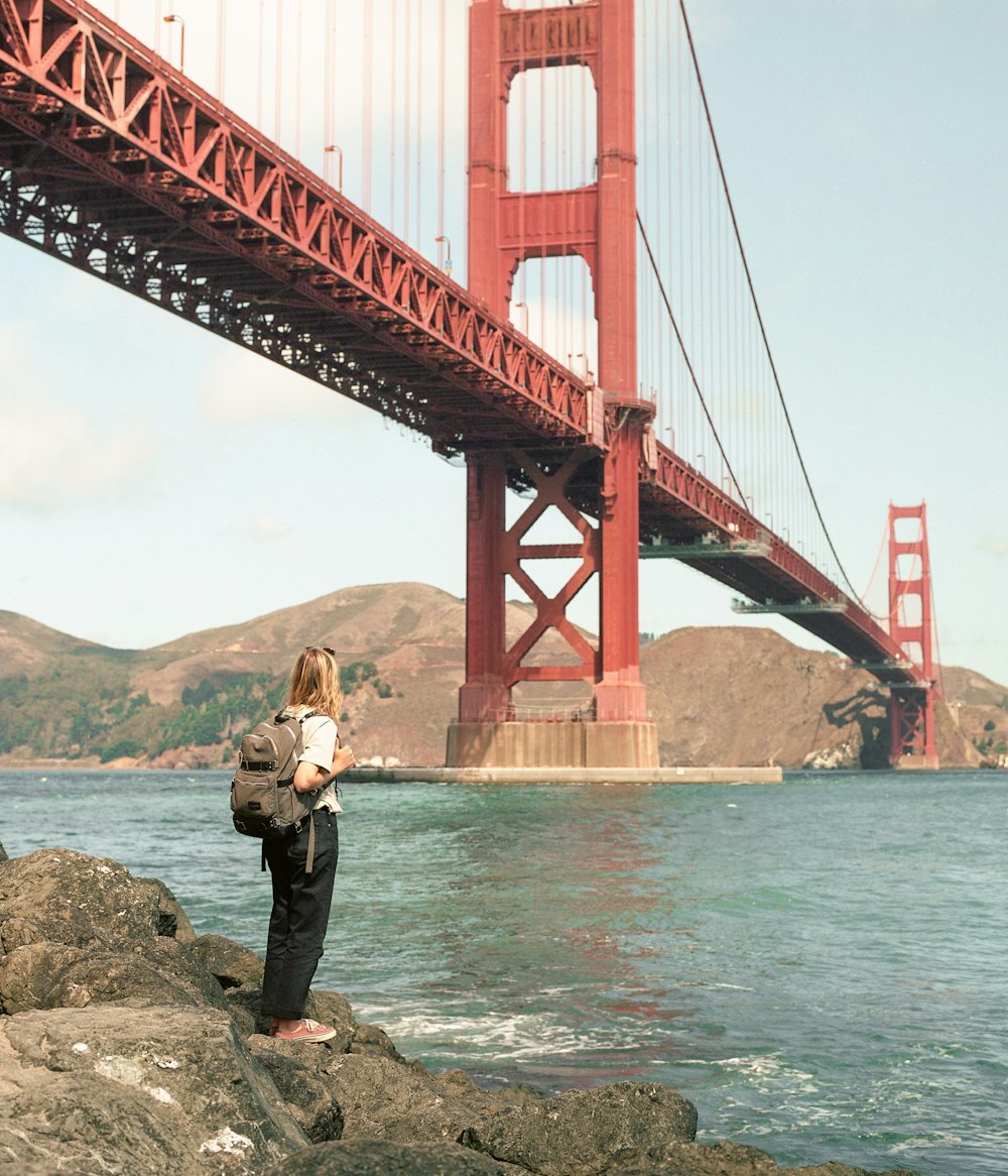 a person standing on rocks near the water and a bridge