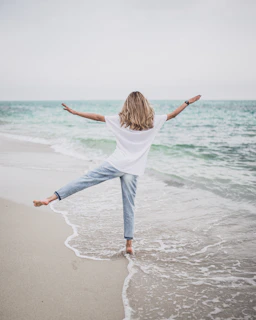 a woman standing on a beach with her arms outstretched