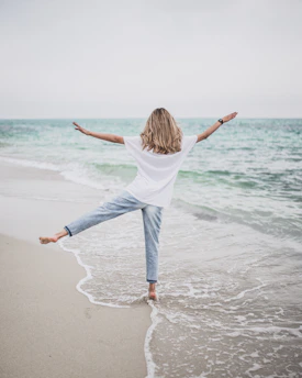 a woman standing on a beach with her arms outstretched