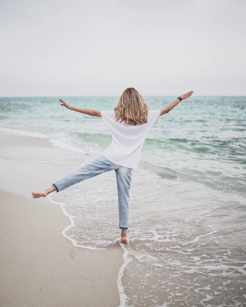 a woman standing on a beach with her arms outstretched