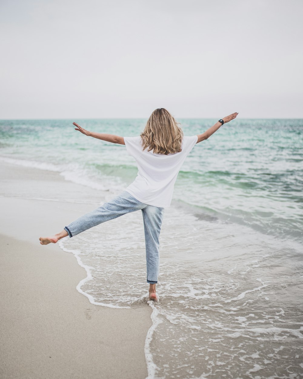 a woman standing on a beach with her arms outstretched