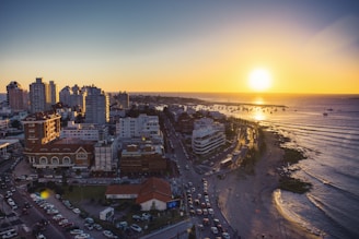 the sun is setting over a city by the ocean