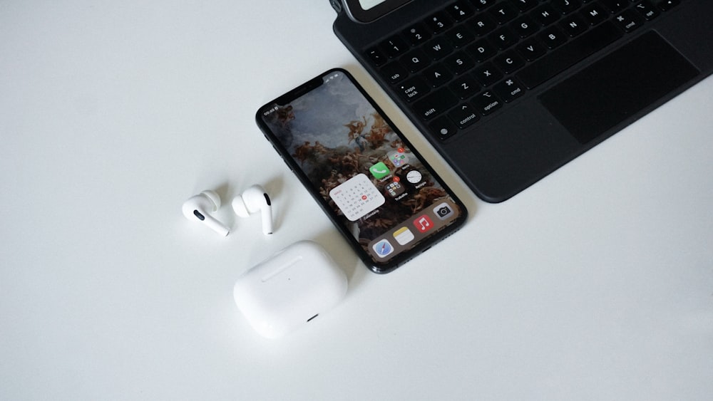 an iphone, ear buds, and laptop on a table